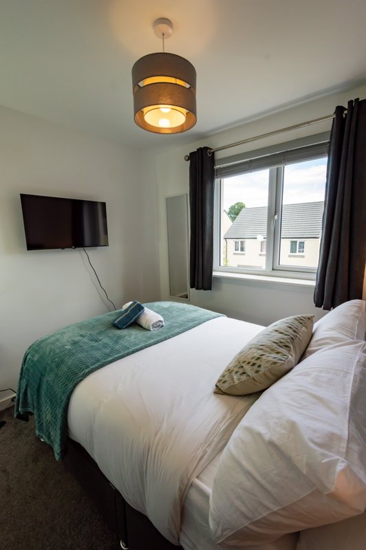 Bright bedroom with double bed, pendant light, wall-mounted TV and window with black curtains