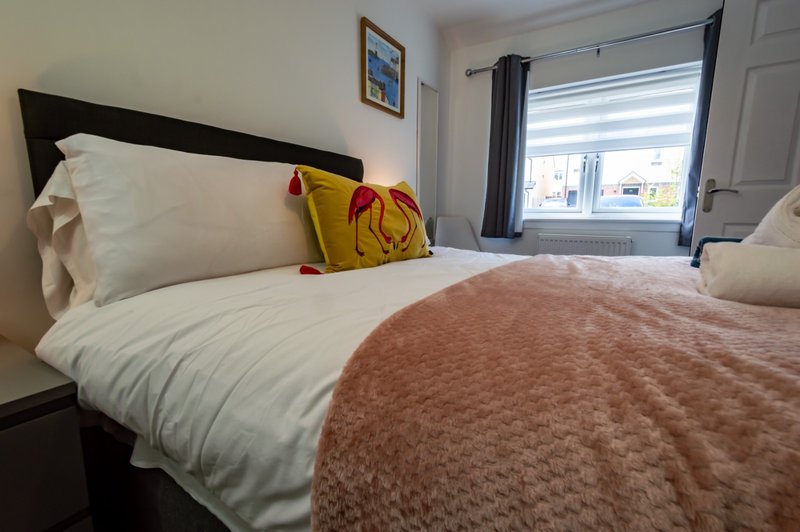 Bedroom with double bed, white sheets, terracotta blanket, decorative pillows and window view