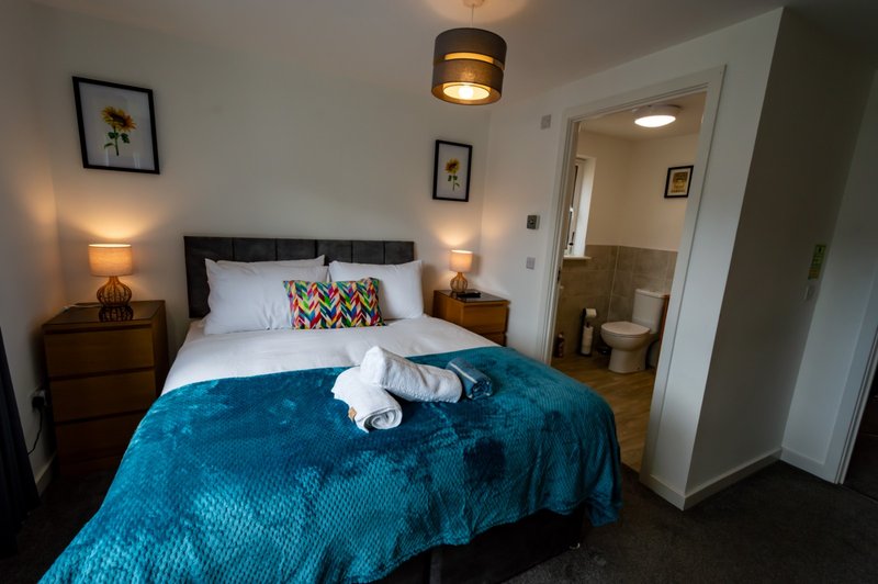 Bedroom with double bed, blue bedspread, wooden nightstands, lamps and ensuite bathroom visible
