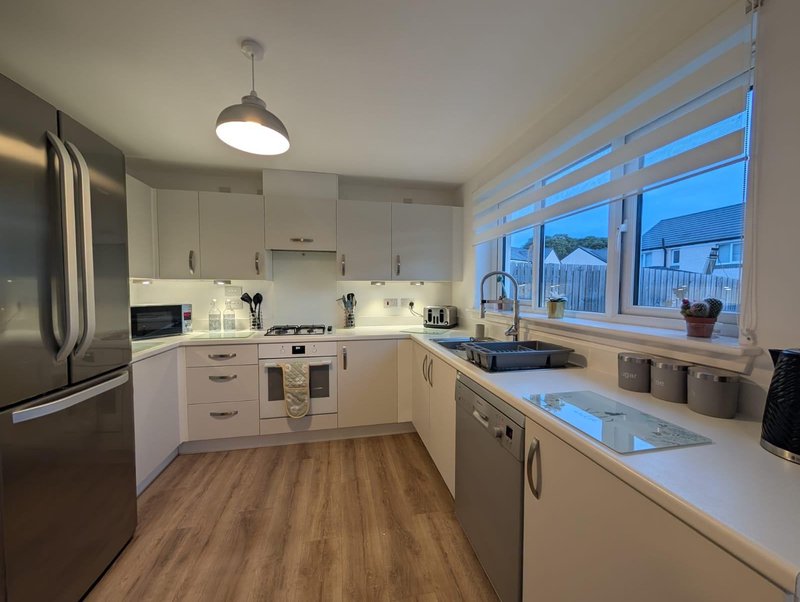 Modern kitchen with white cabinets, stainless steel appliances, wooden floor and window overlooking cityscape
