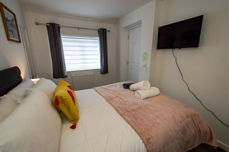 Bedroom with double bed, wall-mounted TV, window with curtains and folded towels