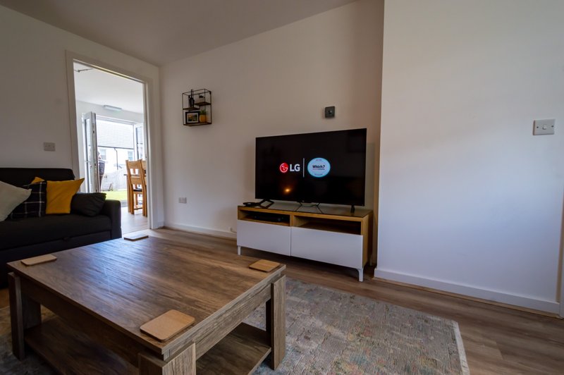 Modern living room with wooden coffee table, TV on stand, and sofa with yellow cushion