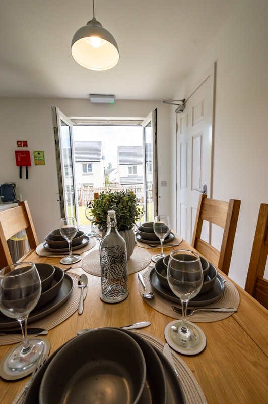 Dining room with wooden table set for four, pendant light, and view to street through open doors