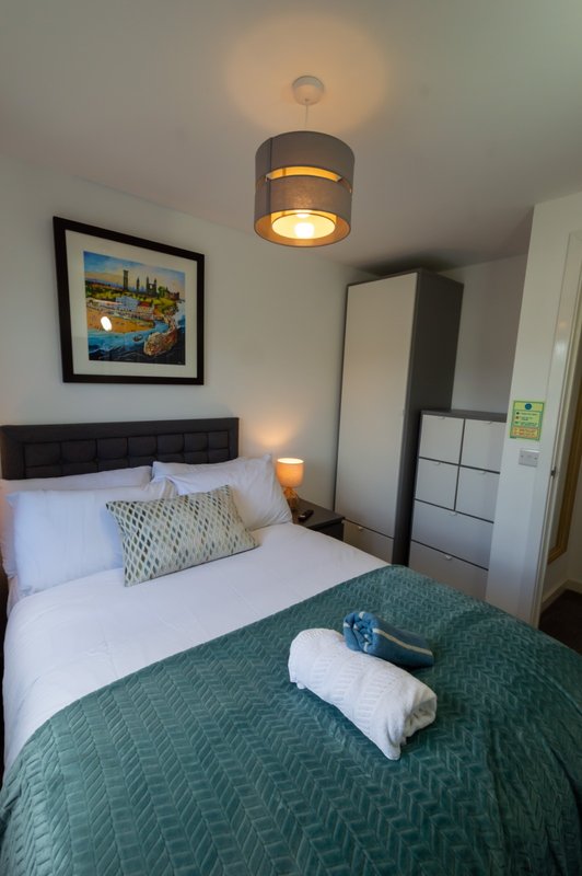 Bedroom with double bed, green throw blanket, pendant ceiling light, framed wall art, and wardrobe