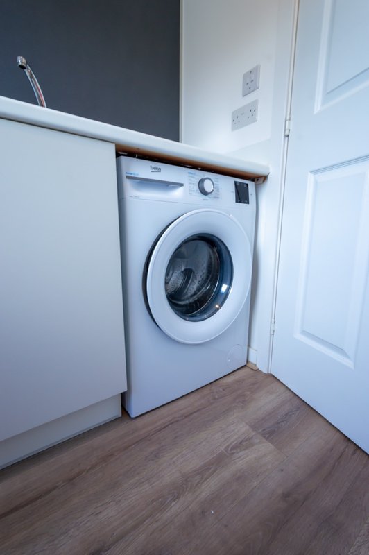 Laundry room with white front-loading washing machine, wooden floor and white door