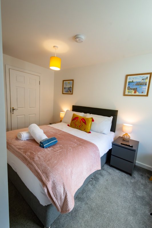 Bright bedroom with double bed, pink bedding, black headboard, bedside lamps and framed wall art