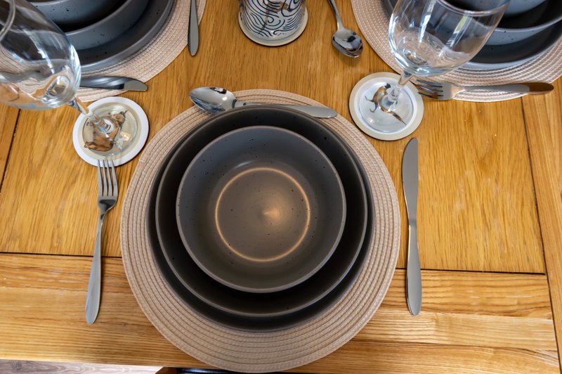 Overhead view of wooden dining table set with black plates, glasses, and cutlery
