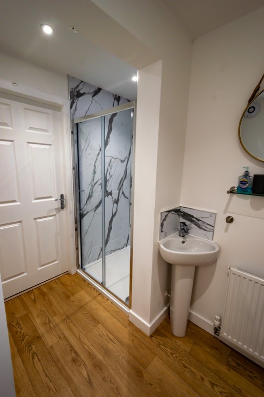 Bathroom with marble-effect shower enclosure, pedestal sink, wooden floor and white door