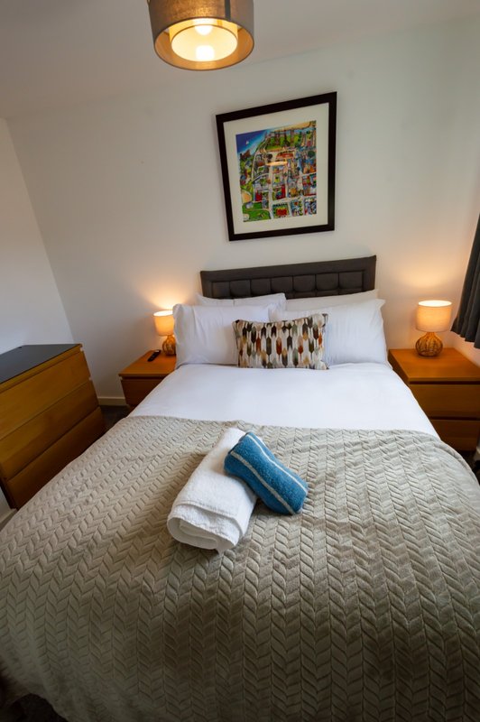 Bedroom with double bed, wooden bedside tables, pendant light, framed wall art and lamps