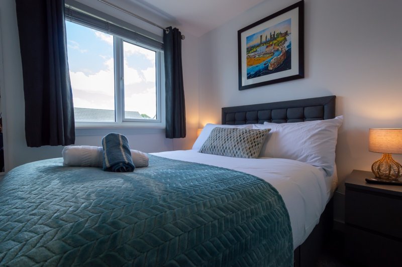 Modern bedroom with double bed, teal bedding, white pillows, and window with sea view