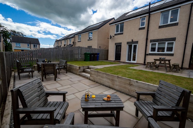 Paved garden terrace with seating area, lawn, and modern townhouses beyond