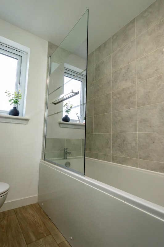 Modern bathroom with glass shower enclosure, white tile surround, and window overlooking garden