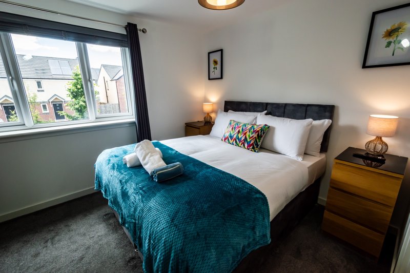 Bright bedroom with double bed, blue throw, wooden nightstands, bedside lamps and window view