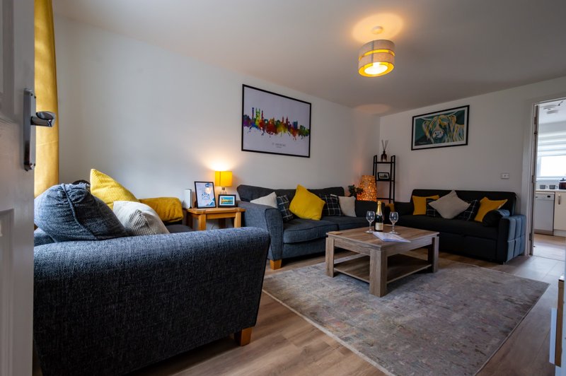 Bright living room with black sofas, yellow cushions, wooden coffee table and framed wall art
