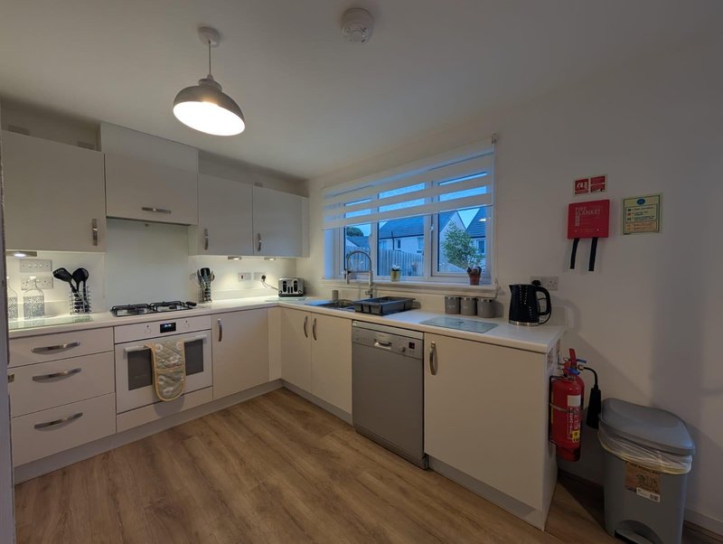 Modern kitchen with white cabinetry, stainless steel appliances, wooden flooring and pendant light