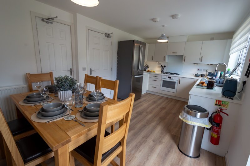 Open-plan kitchen and dining area with wooden table, white cabinetry, and stainless steel appliances