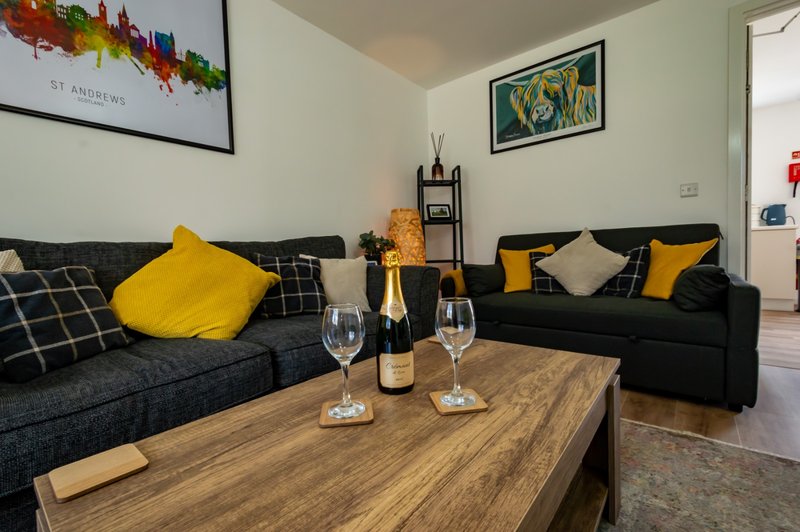Living room with dark sofas, yellow cushions, wooden table, wine bottle and glasses