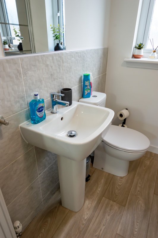 Compact bathroom with pedestal sink, toilet, tile walls and wooden floor