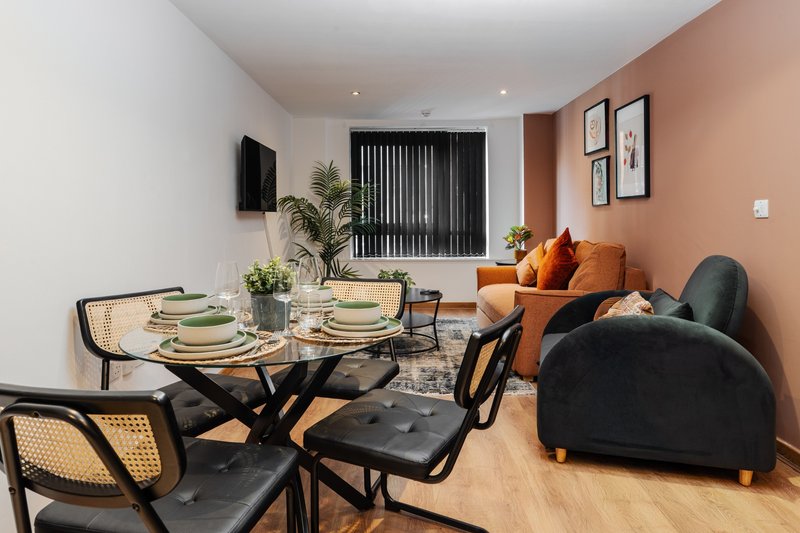 Modern open-plan living and dining area with set dining table, black chairs, orange sofa and potted plants