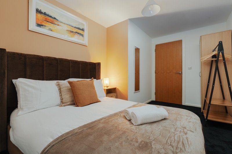 Modern bedroom with double bed, brown headboard, white bedding, orange cushions and warm lighting