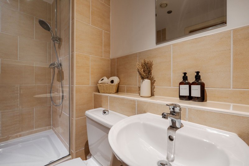 Modern bathroom with beige tile, walk-in shower, white sink and toilet, decorative accessories