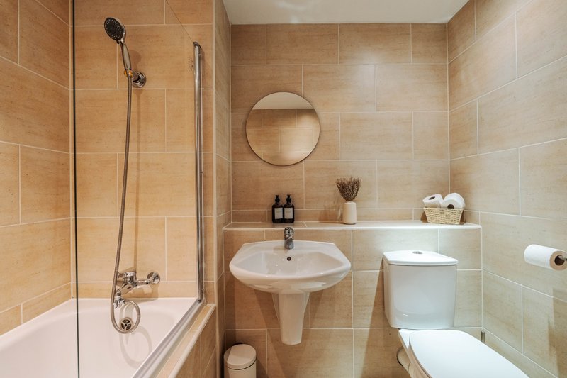 Modern bathroom with pedestal sink, round mirror, shower bath and toilet