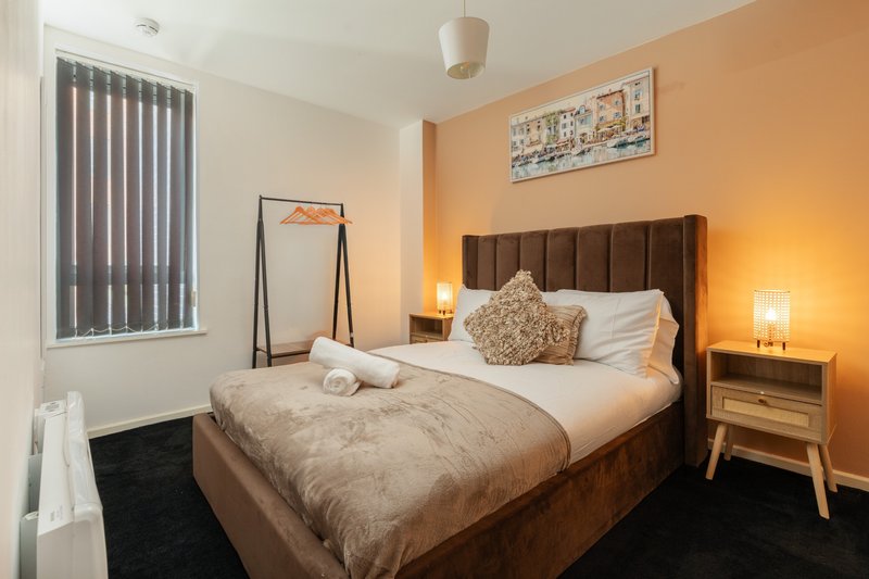 Bedroom with brown upholstered bed, warm orange walls, wooden nightstands and bedside lamps