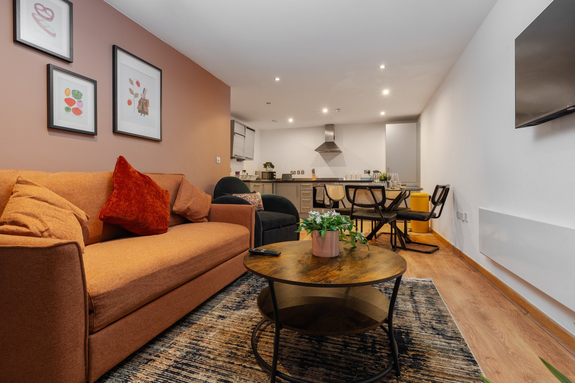 Open-plan living room with orange sofa, wooden coffee table, and kitchen area visible in background