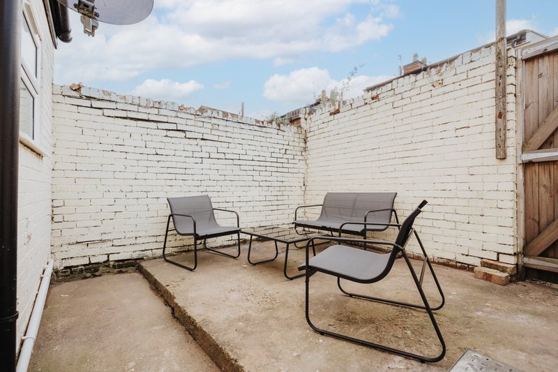 Outdoor patio area with three metal-frame chairs and concrete flooring, enclosed by white brick walls
