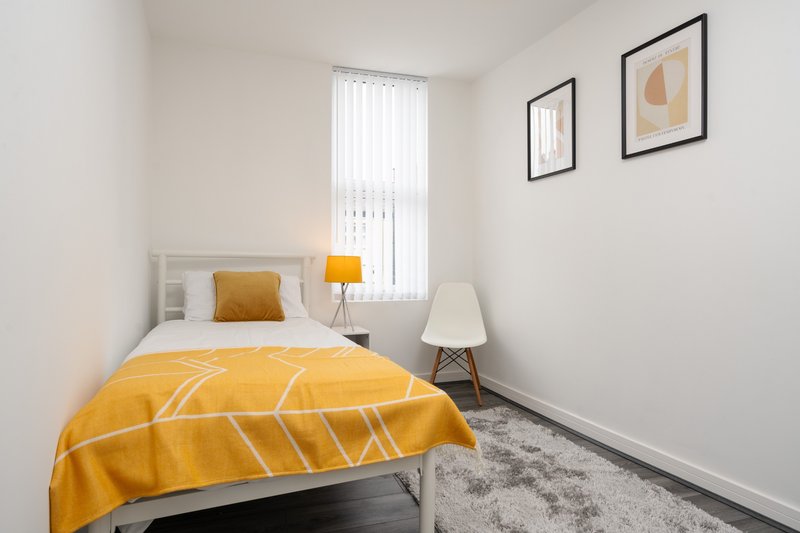 Bright bedroom with single bed, yellow bedding, bedside lamp and framed wall art