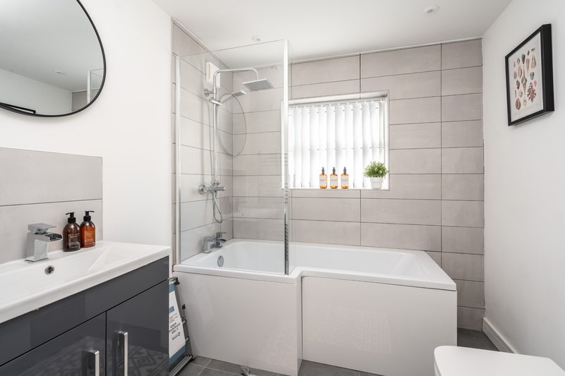 Modern bathroom with walk-in shower, white tile walls, dark vanity unit and circular mirror