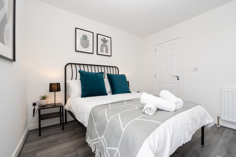 Modern bedroom with metal frame bed, teal cushions, white bedding and side table