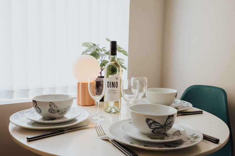 Dining table set with plates, glasses, wine bottle and potted plant by window