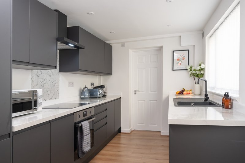 Modern kitchen with dark grey cabinets, white countertops, island, and natural light from window