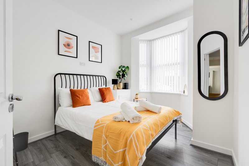 Bright modern bedroom with metal-frame bed, orange bedding, framed wall art and mirror