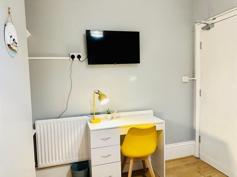 Bedroom workspace with wall-mounted TV, white desk, yellow chair and lamp