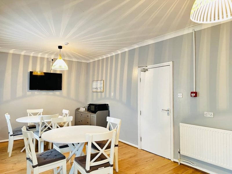 Modern dining area with round white table, striped wallpaper, TV mounted on wall, and wooden flooring