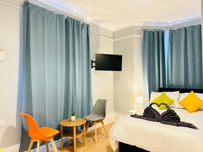 Modern bedroom with double bed, yellow pillows, wall-mounted TV, grey curtains and seating area
