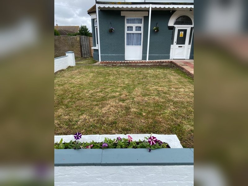 Blue and white beach hut exterior with white-trimmed doors, flower planter, and grass area