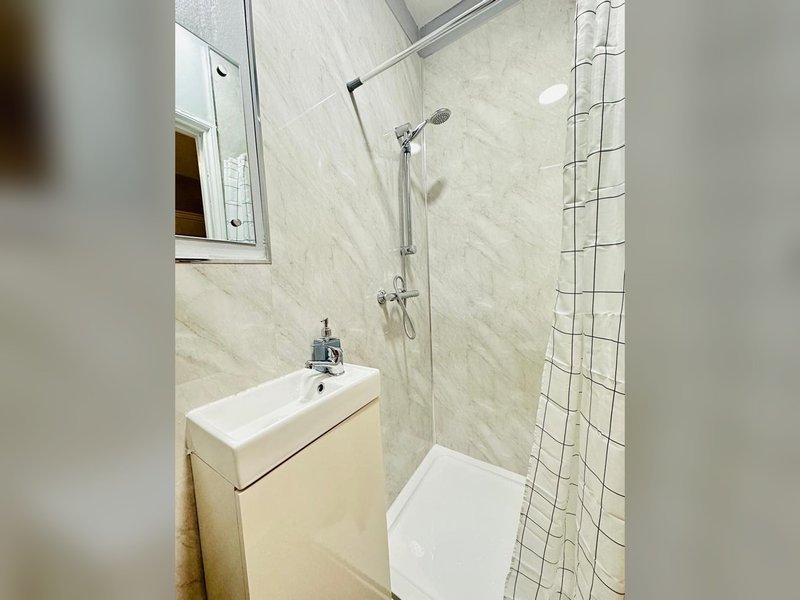 Small bathroom with cream vanity, white sink, shower enclosure and tiled walls