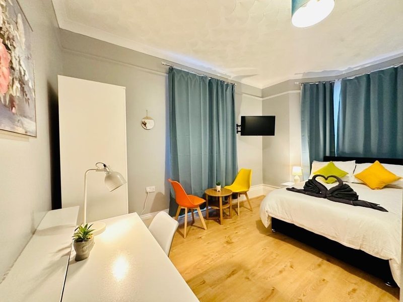 Studio bedroom with bed, dining table, chairs, wooden flooring and teal curtains