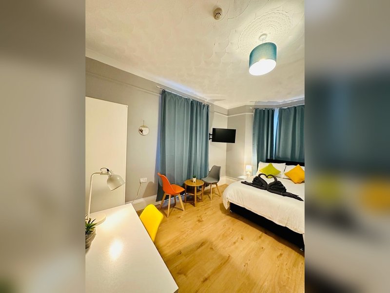 Spacious bedroom with wooden floor, double bed, orange chairs, and window with teal curtains