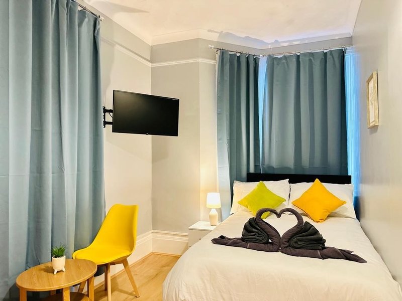 Bedroom with double bed, yellow cushions, wall-mounted TV, green curtains and wooden chair