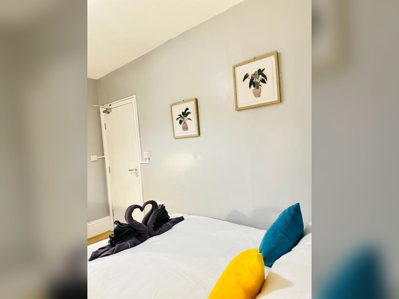 Bright bedroom with white bed, colored pillows, framed botanical art, and white door
