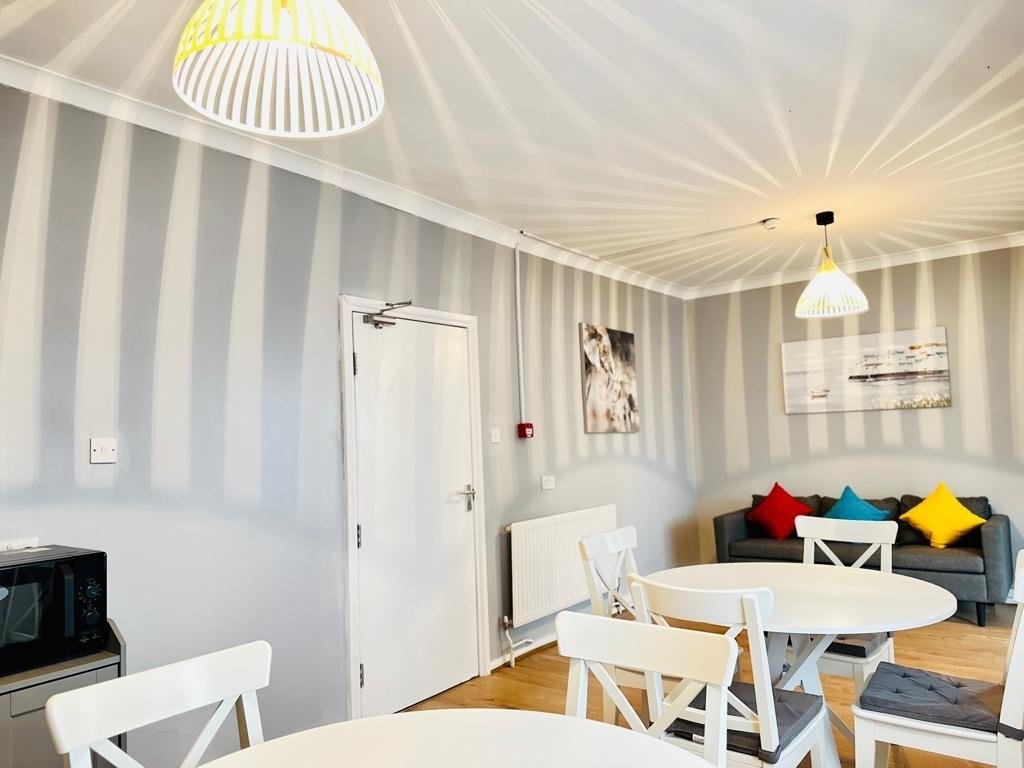 Open-plan dining and living area with striped wallpaper, white furniture, and colorful cushions