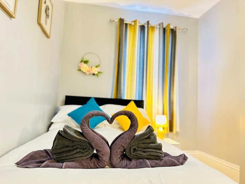 Bedroom with double bed, decorative towel swans, colorful striped curtains and wall art