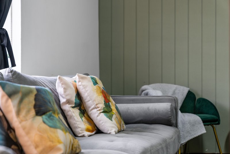 Modern bedroom seating area with gray armchair, decorative pillows, and green paneled wall
