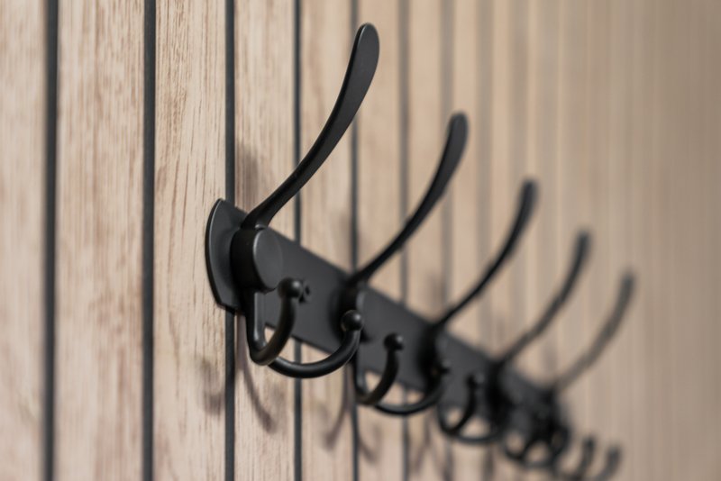 Row of black metal coat hooks mounted on wooden wall paneling