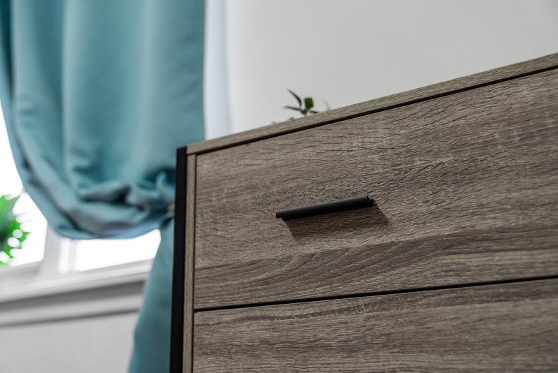 Wooden dresser with dark stain finish near window with teal curtain