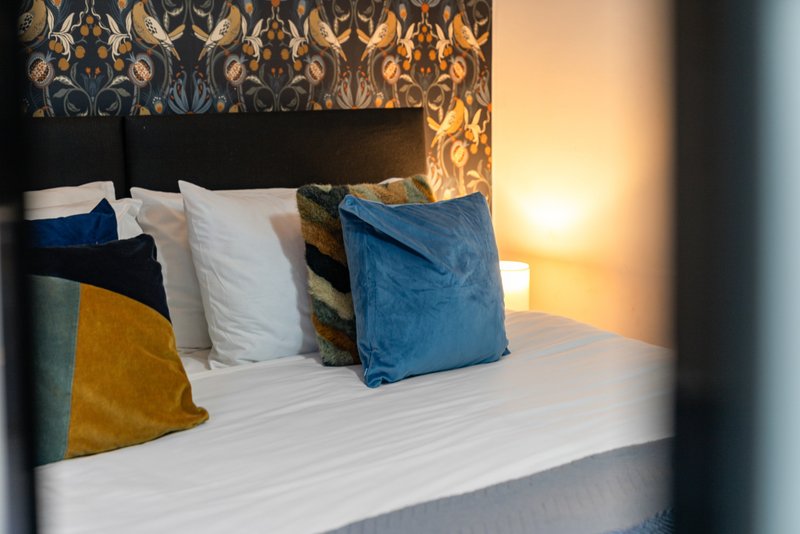 Bedroom with double bed, colorful cushions, patterned headboard and warm lighting